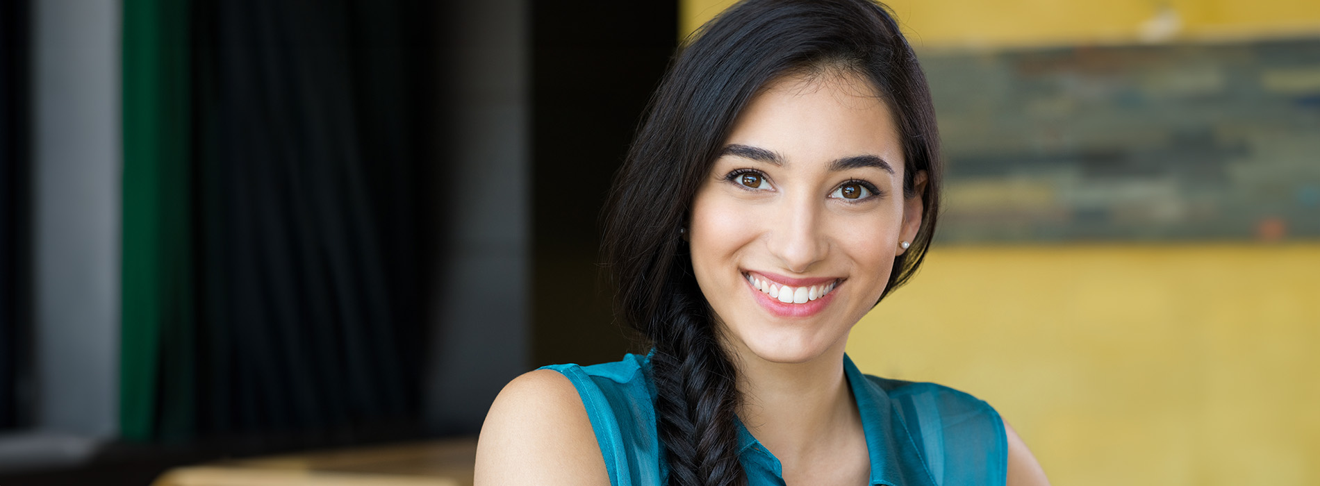 The image is a photograph of a woman with light skin, smiling at the camera. She appears to be in her late twenties or early thirties and has long hair. Her eyes are looking directly at the camera, and she is holding up her index finger near her mouth as if she s making a point or emphasizing something. The background is plain and light-colored, which suggests that this could be a stock photo used for various purposes such as advertising, personal branding, or lifestyle content.